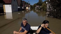 Warga mendayung perahu di antara rumah-rumah yang terendam banjir. 