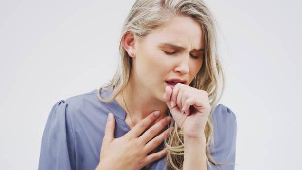 Studio shot of an attractive young woman coughing against a grey background
