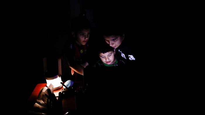 Esther Gualtieri and her sons Rafael and Miguel Diaz Gualtieri look at a screen during a power outage, in Quito, Ecuador September 23, 2024. REUTERS/Karen Toro