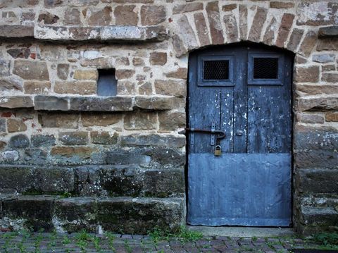 Locked two-toned grey wood paneled entrance to a moss-covered brick building on the outskirts of Hanoi, Vietnam.
