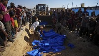 Sebuah buldoser menggali parit di salah satu lahan pemakaman di Khan Younis, sebelum membaringkan semua jenazah yang masing-masing dibungkus kantong plastik biru dan menimbunnya dengan pasir.  