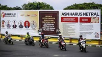 Sejumlah pengendara motor melintas di depan baliho sosialisasi yang terpasang di pinggir Jalan Pemuda Ternate, Maluku Utara, Jumat (27/9/2024).