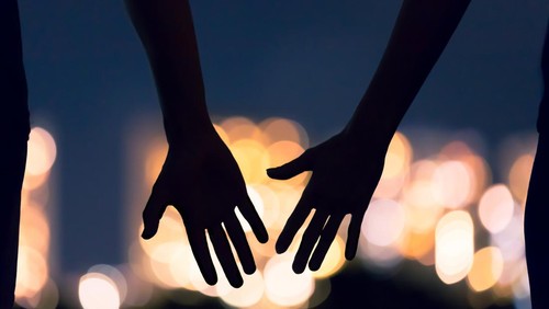 Man and womans hands coming together facing the city night lights.
