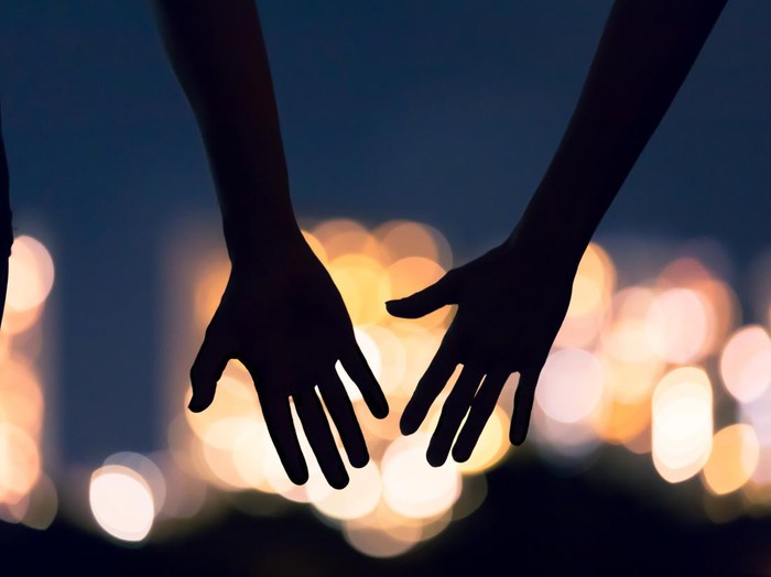 Man and womans hands coming together facing the city night lights.