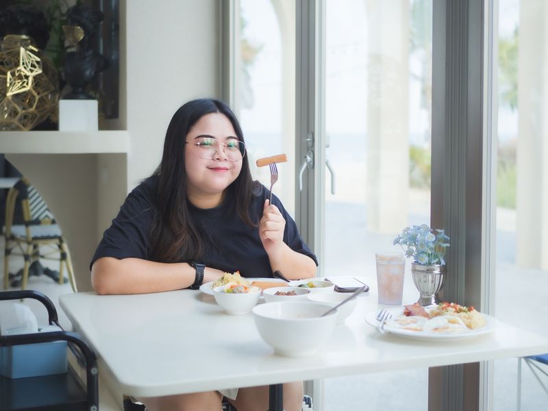 A cheerful, plump Asian woman savors her meal at a restaurant.