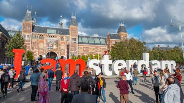 I Am Amsterdam sign in front of the Rijksmuseum with numerous tourists taking selfie pictures in Amsterdam. The Rijksmuseum is dedicated to arts and history in Amsterdam and is the home of various Rembrandt paintings, including the The Night Watch.