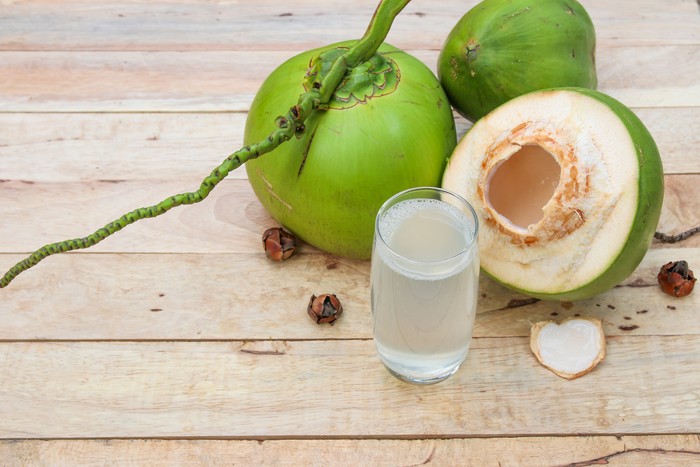 Fresh Coconut Water Drink in glass with coconut leaf on wooden  background