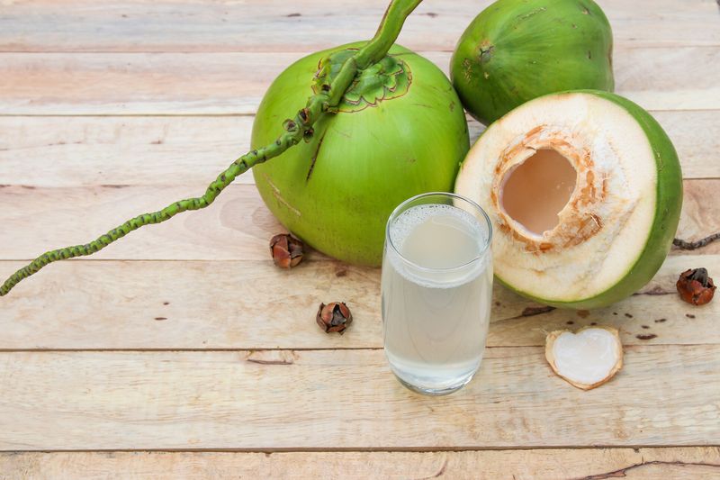 Fresh Coconut Water Drink in glass with coconut leaves on wooden background