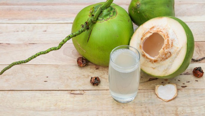 Fresh Coconut Water Drink in glass with coconut leaf on wooden  background