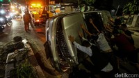 Warga berusaha membalikkan mobil yang terguling di tengah jalan.