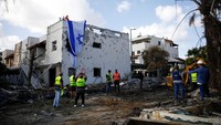 Pria Israel mengibarkan bendera Israel di atas gedung yang rusak akibat roket dari Lebanon saat petugas darurat bekerja di lokasi rumah-rumah yang rusak setelah serangan itu, di tengah permusuhan lintas batas antara Hizbullah dan Israel, di Kiryat Bialik, Israel. Militer Israel mengatakan telah mencegat sejumlah besar dari 180 rudal balistik yang diluncurkan oleh Iran, tetapi ada dampak terisolasi di Israel Tengah dan Selatan. REUTERS/Shir Torem