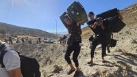 Warga Suriah membawa barang bawaan mereka saat menyeberang dengan berjalan kaki ke Suriah melalui kawah yang disebabkan oleh serangan udara Israel untuk memotong jalan antara pos pemeriksaan Lebanon dan Suriah, di persimpangan Masnaa, di timur Lembah Bekaa, Lebanon. Selain serangan darat, militer Israel juga membombardir Lebanon dengan serangan udara. AP/Samer Husseini