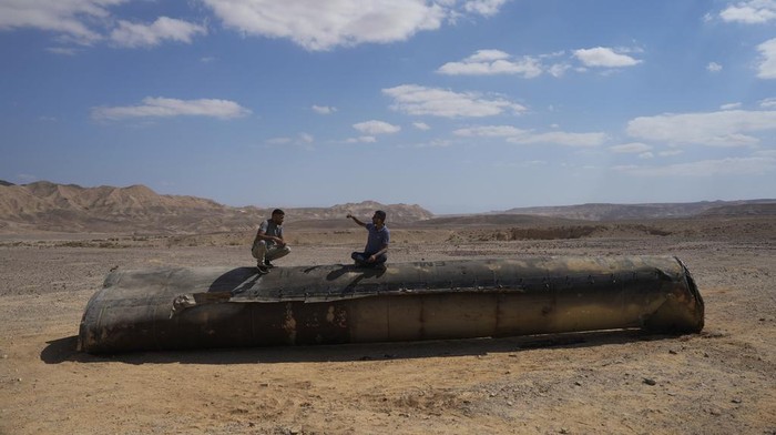 People sit on the debris of an Iranian missile intercepted by Israel, near Arad, southern Israel, Oct. 2, 2024. (AP Photo/Ohad Zwigenberg)