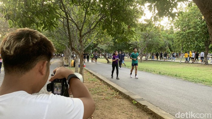 Bhani, fotografer jalanan, sedang memotret masyarakat berolahraga di Lapangan Niti Mandala Bajra Sandhi, Denpasar, Bali, Minggu sore (6/10/2024). (Rizki Setyo/detikBali)