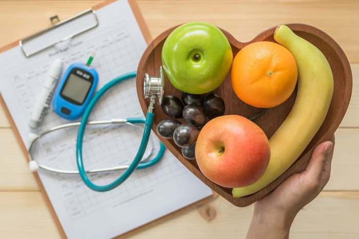 Cholesterol diet and healthy food nutritional concept with clean fruits in heart dish with nutritionist monitoring, blood sugar control record with measuring tool kit