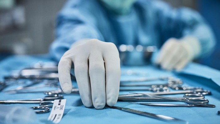 Surgeon picking up surgical tool from tray. Surgeon is preparing for surgery in operating room. He is in a hospital.