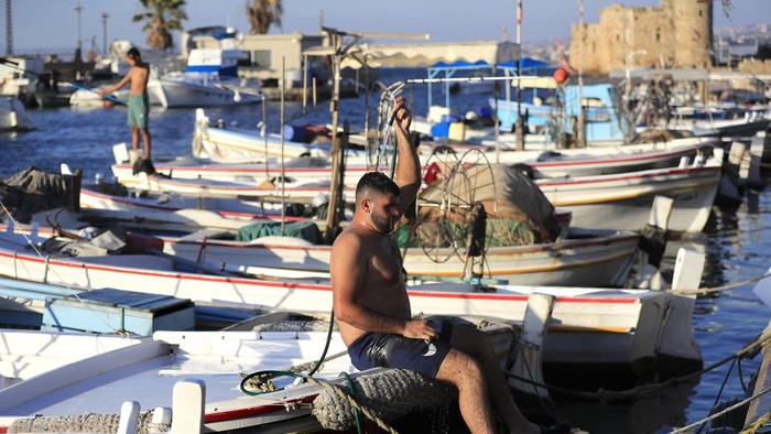 Nelayan Lebanon Tak Bisa Melaut Imbas Israel Serang Hizbullah A Lebanese fisherman cools himself as he sits on his boat after the Israeli army ordered fishermen and people using any kinds of boats not to sail along an area over 50 kilometers (31 miles) from the Israeli border, in the southern port city of Sidon, Lebanon, Tuesday, Oct. 8, 2024. (AP Photo/Mohammed Zaatari)