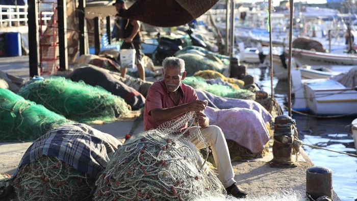A Lebanese fisherman cools himself as he sits on his boat after the Israeli army ordered fishermen and people using any kinds of boats not to sail along an area over 50 kilometers (31 miles) from the Israeli border, in the southern port city of Sidon, Lebanon, Tuesday, Oct. 8, 2024. (AP Photo/Mohammed Zaatari)