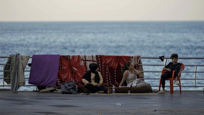 People stand next to a tent set up as a temporary shelter by a displaced family fleeing the Israeli airstrikes in Dahiyeh, in front the Rawcheh Sea Rock, in Beirut, Lebanon, Tuesday, Oct. 8, 2024. (AP Photo/Bilal Hussein)