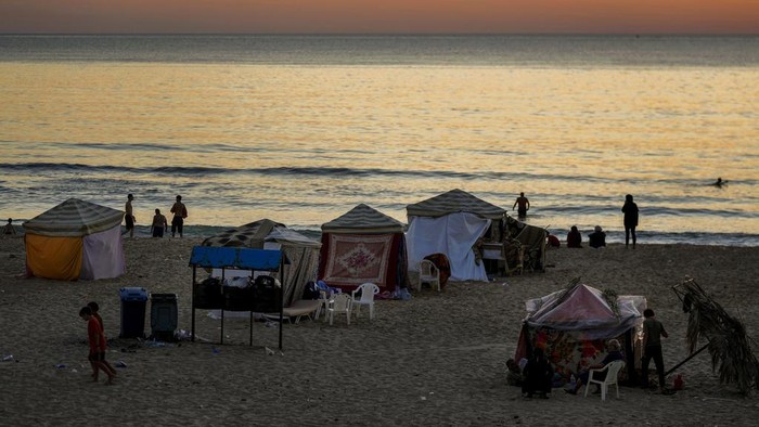 People stand next to a tent set up as a temporary shelter by a displaced family fleeing the Israeli airstrikes in Dahiyeh, in front the Rawcheh Sea Rock, in Beirut, Lebanon, Tuesday, Oct. 8, 2024. (AP Photo/Bilal Hussein)