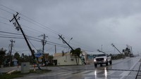 Mobil melintas di dekat tiang listrik yang patah dengan kabel yang menjuntai.  