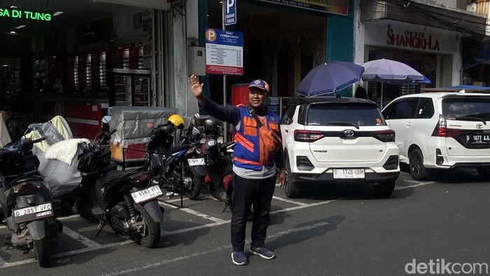 Firman ketika melakukan pekerjaannya sebagai juru parkir di Jalan ABC, Kota Bandung.