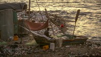 Seorang nelayan memperbaiki jaring di atas perahu.