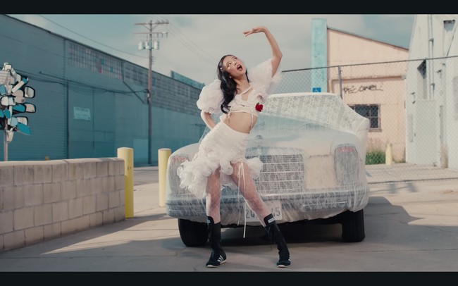 Tampil dengan gaya coquette. Jennie BLACKPINK mengenakan kostum putih rancangan Kitschy Couture. Dengan detail atasan crop top berlengan balon dan tambahan stoking. Dia memberikan sentuhan sporty dengan koleksi sepatu Adidas Japan VH Shoes seharga Rp 2,1 juta. Foto: dok. YouTube JENNIE