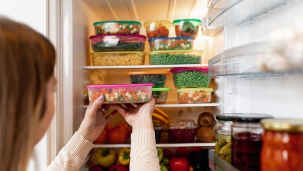 Close up shot of woman taking container with frozen mixed vegetables from refrigerator while looking at camera.