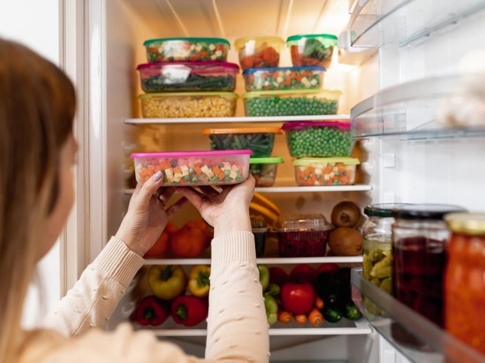 Close up shot of woman taking container with frozen mixed vegetables from refrigerator while looking at camera.