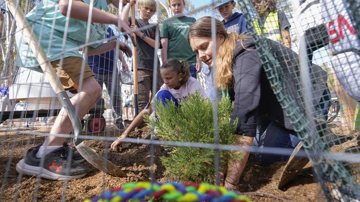 Santiago parent volunteer Stacie Aguesse, right, helps students plant a small Giant Sequoia tree from NASA's Artemis I Mission's tree seeds that traveled around the moon twice, as NASA scientists, JPL engineers, US Forest Service representatives, and teachers join Santiago STEAM Magnet Elementary School students at a ceremony to plant it after the school was honored in the spring of 2024 to become NASA Moon Tree Stewards in Lake Forest, Calif., on Monday, Oct. 14, 2024. (AP Photo/Damian Dovarganes)