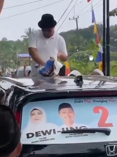 Tangkapan layar video viral seorang pria yang membagikan uang ke warga di atas mobil.
