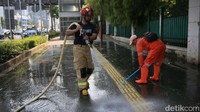 Petugas pemyemprotkan air ke trotoar yang telah disikat.  