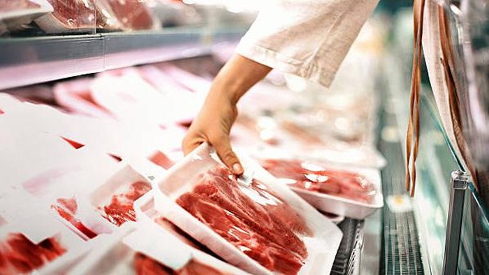 Closeup side view of unrecognizable woman chossing some fresh meat at local supermarket. The meat is cut into chops and packed into one pound packages. She has reached for a package of beef sirloin steaks.