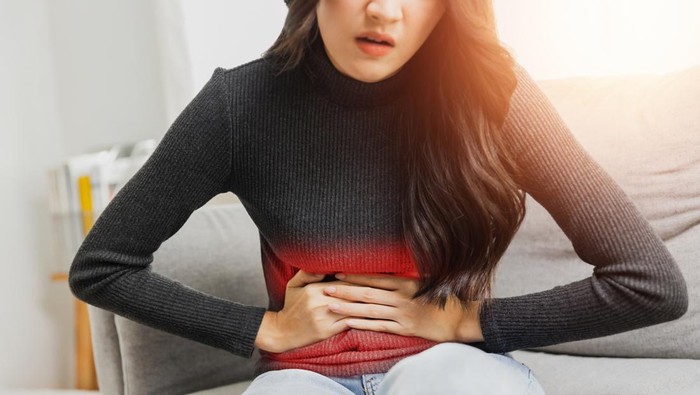 Ilustrasi asam lambung atau sakit perut Young woman suffering from strong abdominal pain while sitting on sofa at home