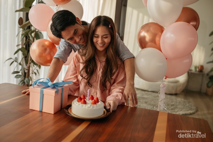 Mid-adult man hugs his wife as they celebrate her birthday with a cake and present.