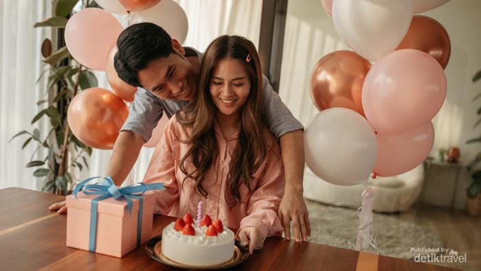 Mid-adult man hugs his wife as they celebrate her birthday with a cake and present.