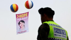 Sebuah plakat yang merayakan keluarnya anggota boy band K-pop BTS, J-Hope, dari wajib militer dikibarkan saat seorang polisi militer berjaga di luar pangkalan militer.
