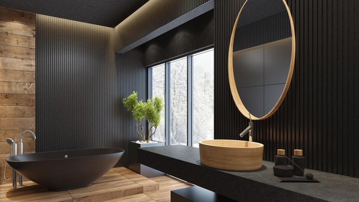 contemporary minimalist bathroom with black wooden walls and large grey matte and wood effect tiles. 
round mirror with wooden frame is on the wooden black wall. 
round grey stone washbasin and stainless steel basin tap is on top of the grey stone vanity unit with three drawers.
freestanding black stone bathtub and floor mounted inox tap is on a platform with wood effect tiles. 
long floor tiles with wood effect. black ceiling with strip cove lighting and embedded spotlights.