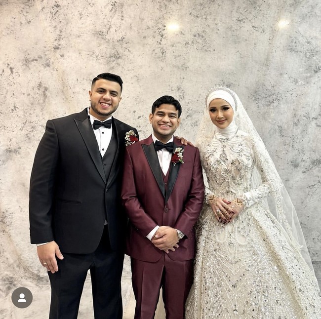 Turut hadir di acara resepsi sang kakak, Fadil tampil mengenakan setelan jas berwarna merah. Ia pun berpose bersama kedua mempelai. Foto: Instagram