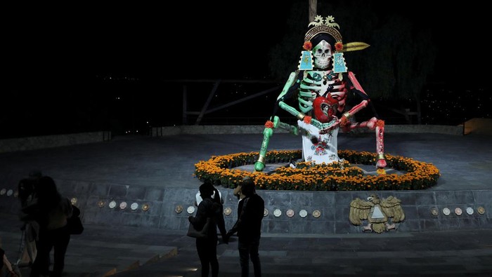 Instalasi Tengkorak Raksasa Semarakan Peringatan Hari Kematian di Meksiko People walk near marigold fields and a giant skeleton figure, built by local artisans representing Mexican bandit-turned-revolutionary Francisco