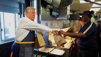 Dikelilingi kamera, Trump mencelupkan keranjang kawat berisi kentang ke dalam minyak panas sebelum memberi garam dan membagikannya kepada pelanggan melalui jendela drive-thru restoran.