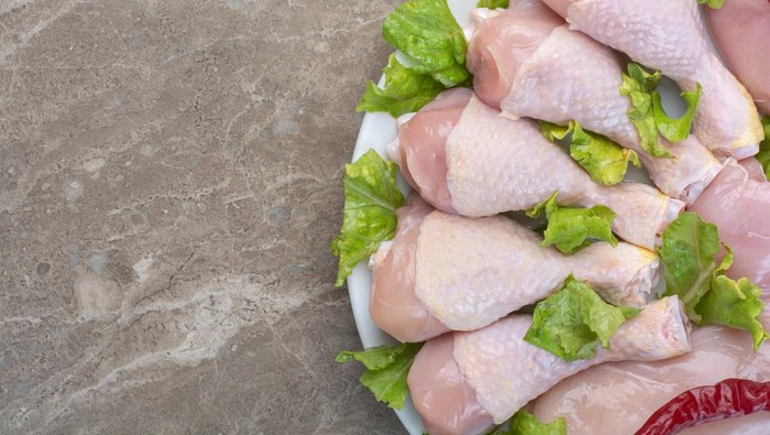 Daging paha ayam mentah yang disajikan di piring dengan daun selada dan cabai.