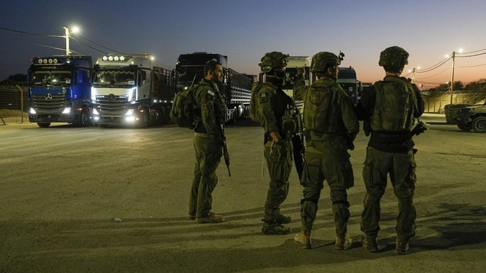 Israeli soldiers stand near trucks carrying humanitarian aid just before they cross into the Gaza Strip at Erez crossing in southern Israel, Monday, Oct. 21, 2024. (AP Photo/Tsafrir Abayov)