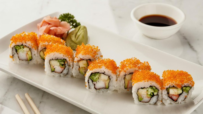 Sushi dengan telur ikan disajikan di piring ditemani sumpit, wasabi, dan kecap