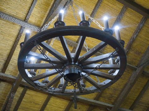 antique wooden chandelier made with antique cart wheel base, hanging from the ceiling of the house with exposed wooden beams