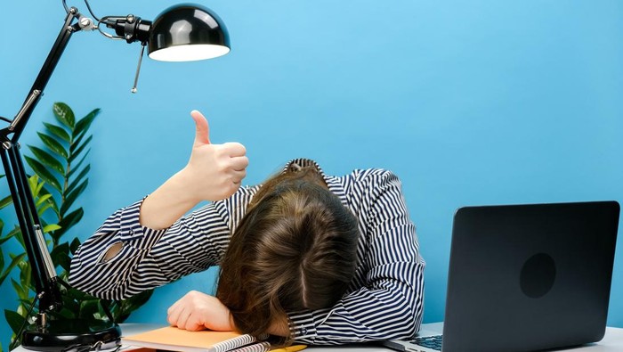 Tired exhausted secretary employee business woman in shirt sitting work sleep laid her head down on office desk with pc laptop show thumb up gesture, isolated on blue color background wall in studio