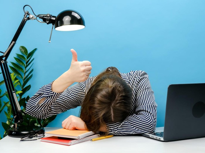 Tired exhausted secretary employee business woman in shirt sitting work sleep laid her head down on office desk with pc laptop show thumb up gesture, isolated on blue color background wall in studio