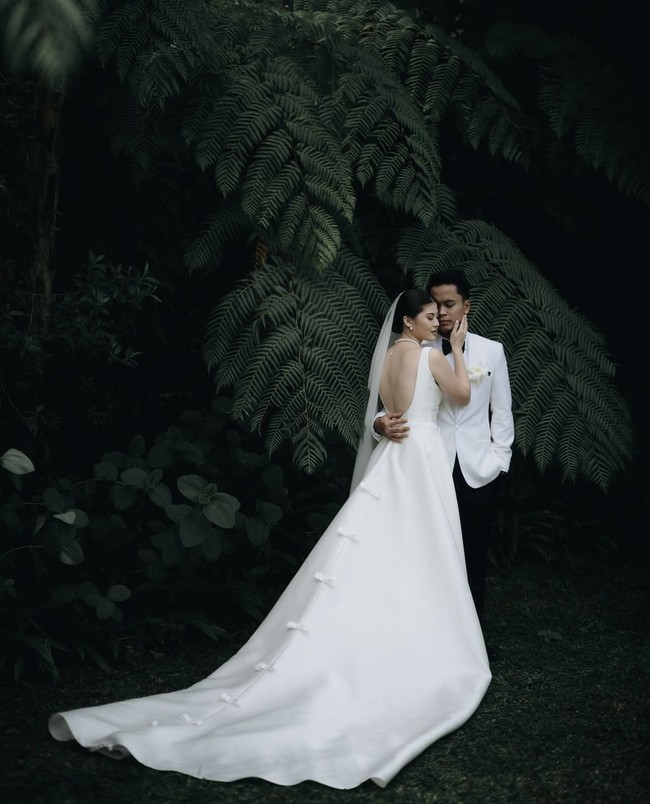 Anthony dan Mitzi tampil kompak dalam balutan busana pengantin berwarna putih. Mitzi memilih gaun backless berekor tanpa lengan. Sementara Anthony mengenakan jas putih dipadukan dasi kupu-kupu dan celana panjang hitam. Foto: Instagram/@sinisukanthony