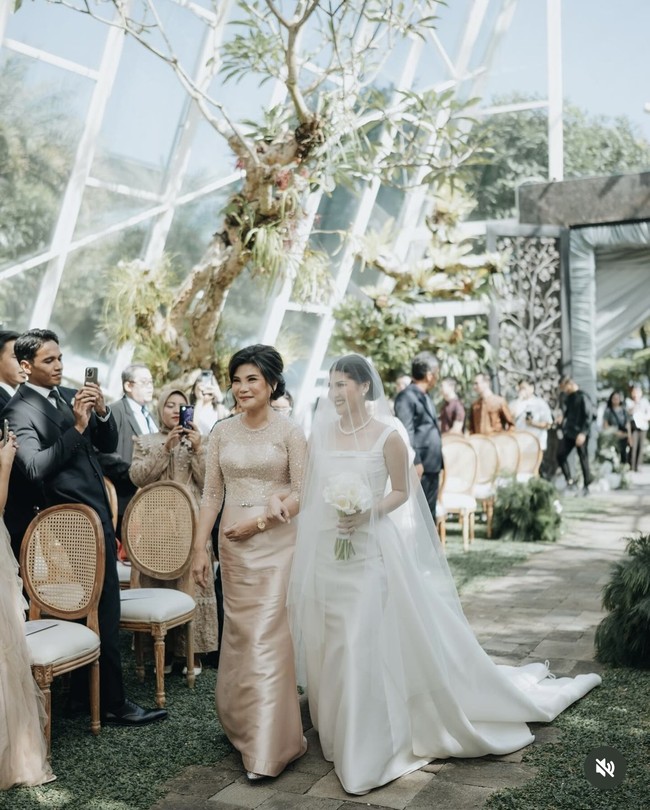 Mitzi tampil cantik menawan berjalan masuk didampingi sang bunda. Mengenakan veil panjang, penampilan Mitzi kian menawan dengan kalung dan sepasang anting mutiara. Foto: Instagram/@sinisukanthony